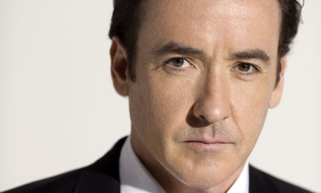John Cusack with a serious expression wearing a suit and tie